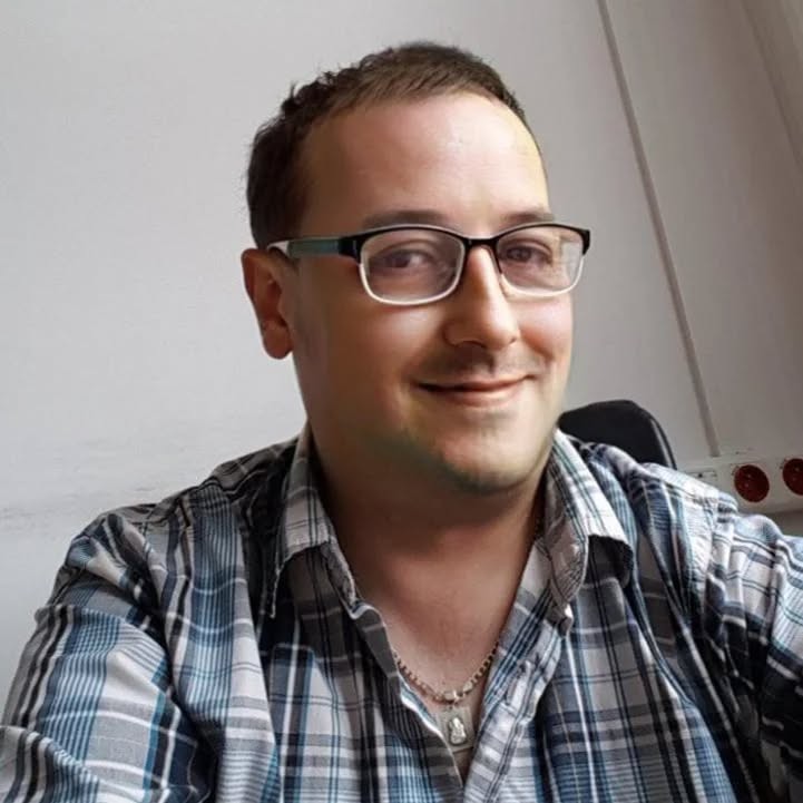 Mariusz Piotr Mączka – portret osobisty, uśmiechnięty, w okularach i koszuli w kratę, zdjęcie wykonane w naturalnym świetle.